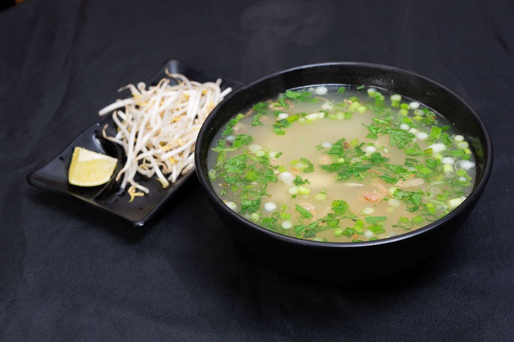 Bowl of pho broth with green onion next to a plate of bean sprouts and lime