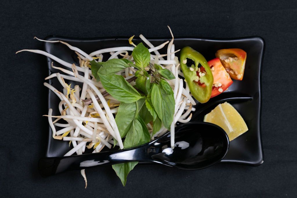 Garnish plate with bean sprouts, basil, lime and jalapeño